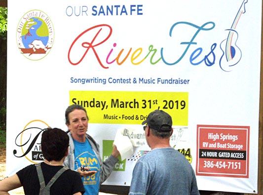 Merrillee in front of the Riverfest poster giving information to two visitors